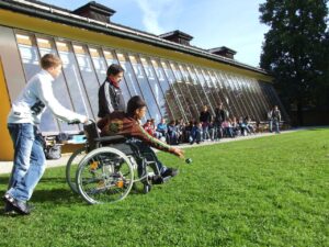 People in wheelchairs participating in an outdoor group activity on a sunny day.